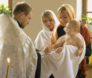 Священник помазует младенца священным миром в Таинстве Миропомазания